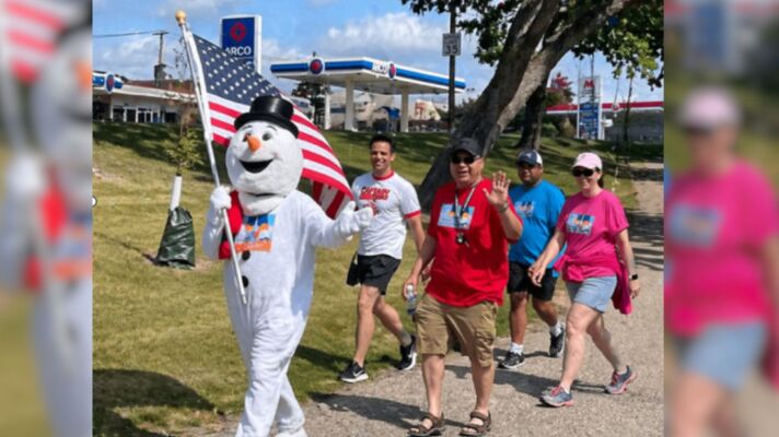 People walking on a trail with a person in a snowman costume leading the way.