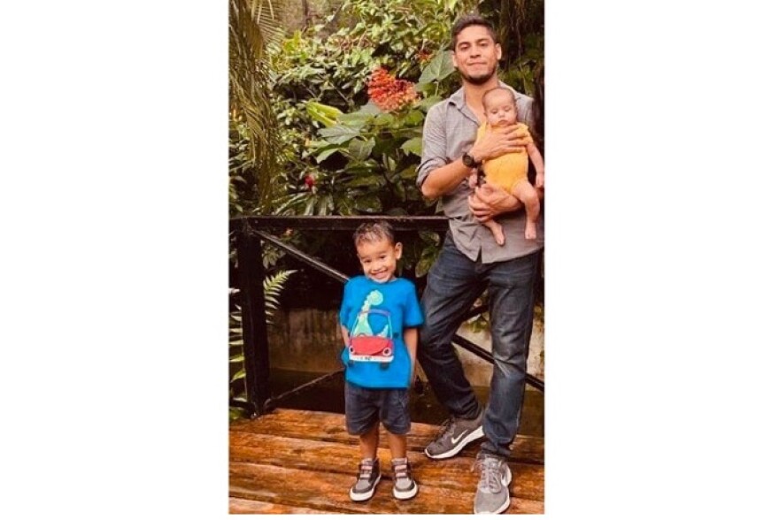 Man with his children: a young child next to him and holding a baby. 