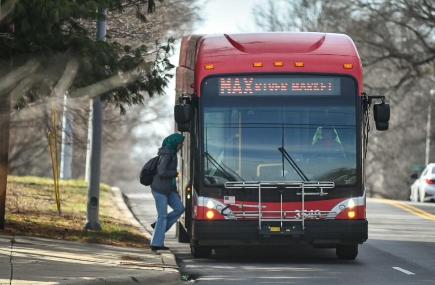 A red commuter bus sits on a city street. A passenger is about to step on.