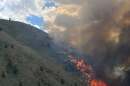 A brushfire burns in the hills just outside Hailey, ID, with bright orange flames and dense black smoke rising over a mountain. 