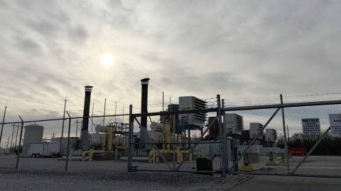 A chain link fence stands in front of the Columbia gas power plant, made up of a variety of pipes and metal boxes. 