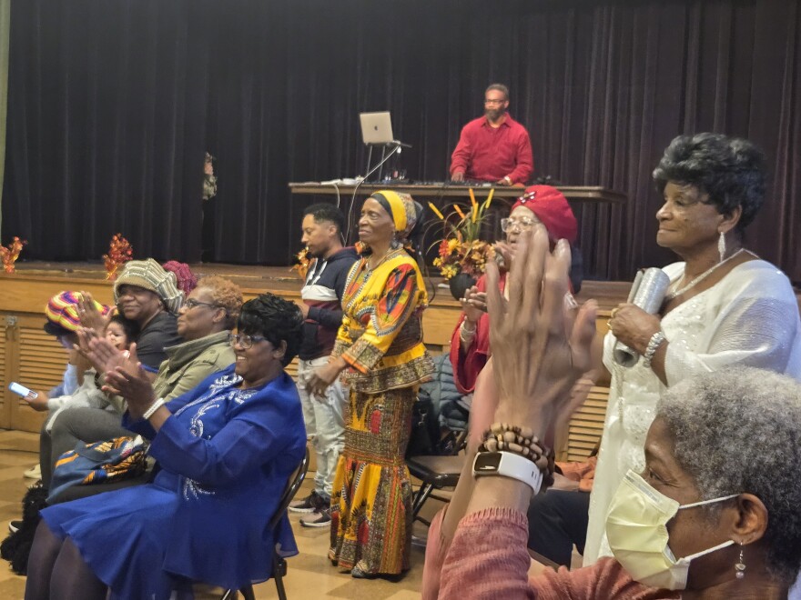 Women stand up in fashionable outfits clapping for the catwalkers.