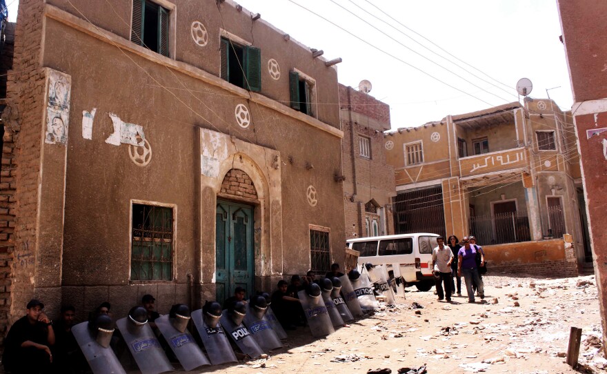 Egyptian riot police sit in the shade by damaged buildings as people walk through debris from the aftermath of clashes on Aug. 1 between Christians and Muslims in Dahshour, on the outskirts of Cairo. The violence was sparked by a dispute between a Muslim and Christian over laundered clothing.