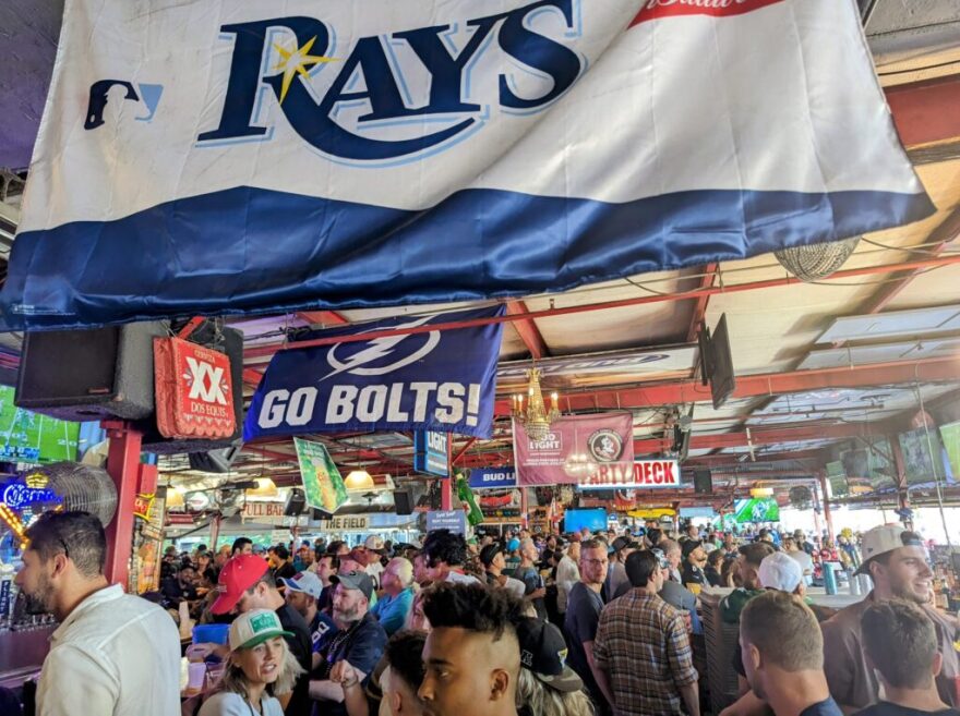 Overview of a crowd inside a sports bar with a large Rays banner hanging off the ceiling and a smaller Go Bolts! banner in the middle