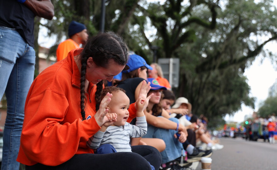 Ashley Mathena with her son, Elliot sitting by the curb to watch the University of Florida Homecoming parade in Gainesville, Friday, Oct. 9, 2026. (Alessia Lavayen/WUFT News)