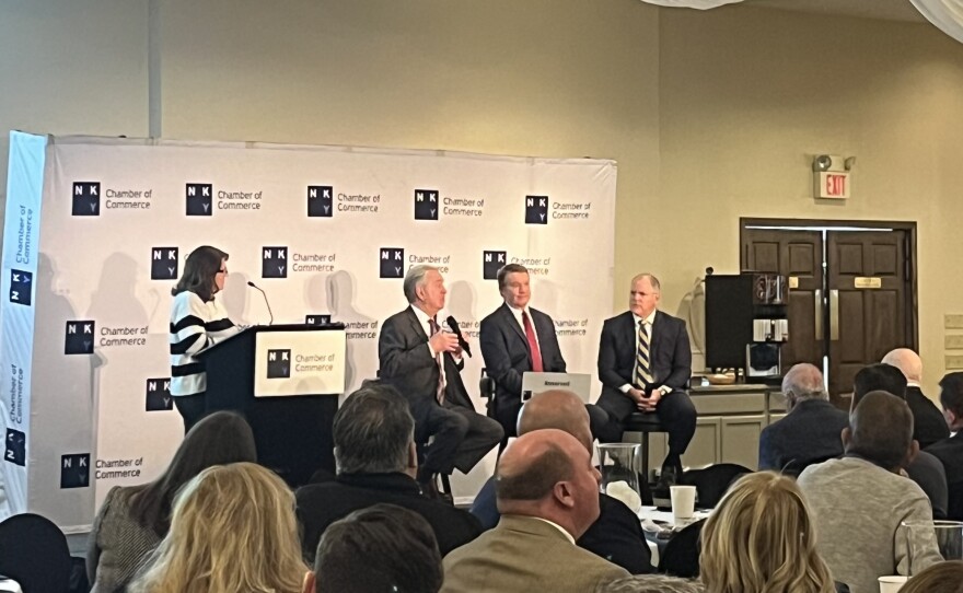 A woman stands at a podium and three men sit beside her for a panel discussion.