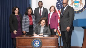 Governor Gretchen Whitmer sits at a table to sign a bill. She is surrounded by several people, including Lt. Gov. Garlin Gilchrist.