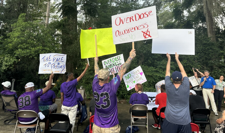 Attendees come together and raise their posters as they’re recognized for walking 5,501 steps in honor of loved ones lost to addiction. (Mackenzie Davis/WUFT News)