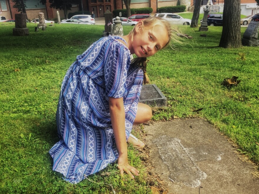 Laila Ericksen, 10, kneels at one of the historic grave markers on the grounds of St. John Chrysostom church, in Delafield, Wis. The town's founder, Charles Delafield, is buried here.