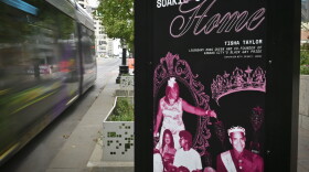 A black and purple sign sits on a city sidewalk. There are several photos of people on it. The sign reads "Soakie's Was Home."