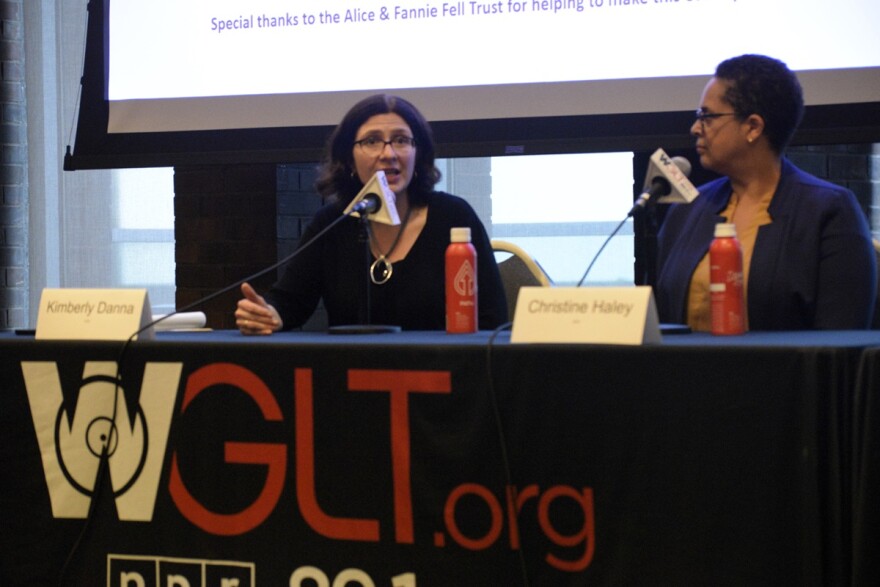 Two women sitting at a table with microphones, engaged in a discussion during a public forum