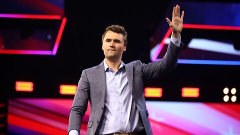 Man in suit stands on stage and waves