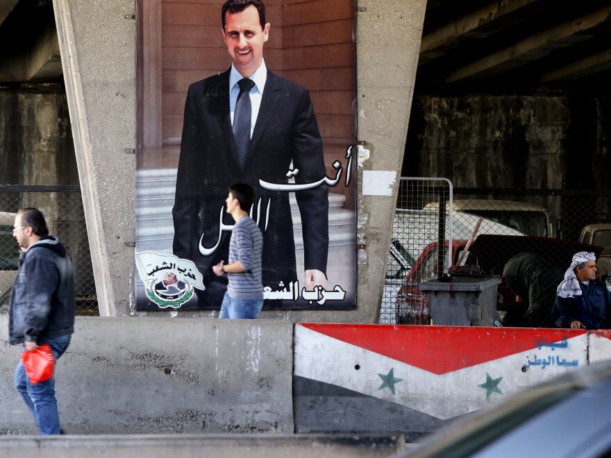 Syrian men walk past a poster bearing a portrait of President Bashar Assad in Damascus, on Feb. 27, 2016.