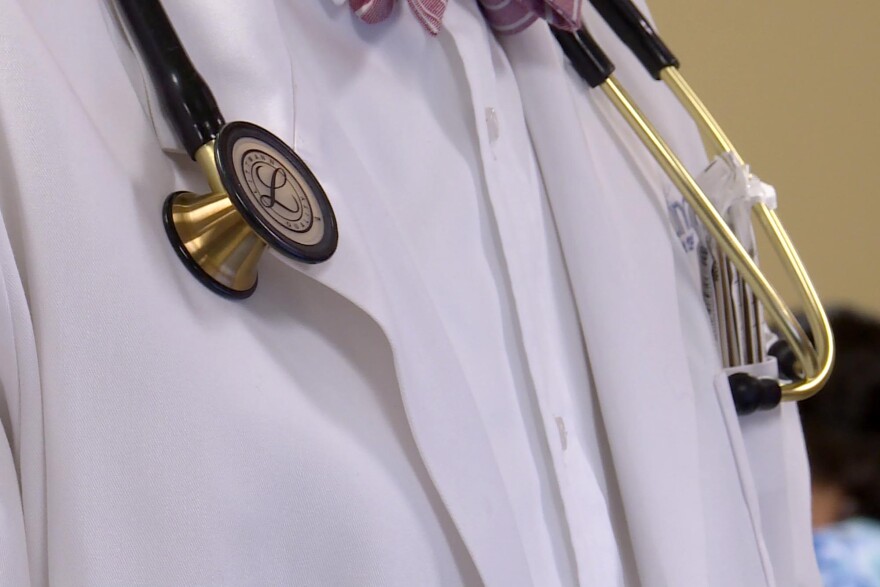 A medical professional's torso is show in a photo. A white lab coat and stethoscope are visible.