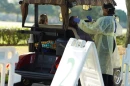 A nurse in a mask and and protective suit stands beside a golf cart that pulled up at a drive-thru test site. Two women sit in the cart. The nurse holds a swab up to one of the women's noses preparing to test her for COVID-19.