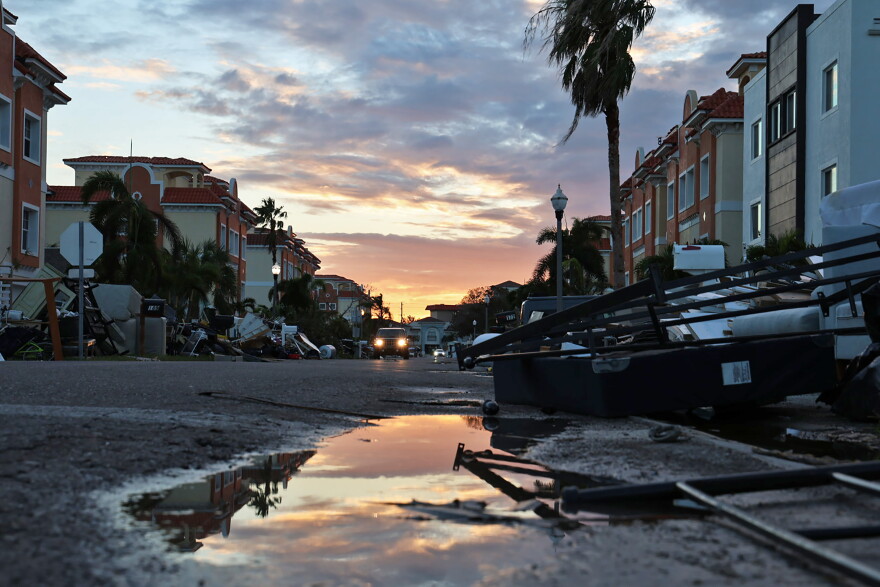 A neighborhood with flooding and debris in the street, and a sunset in the background