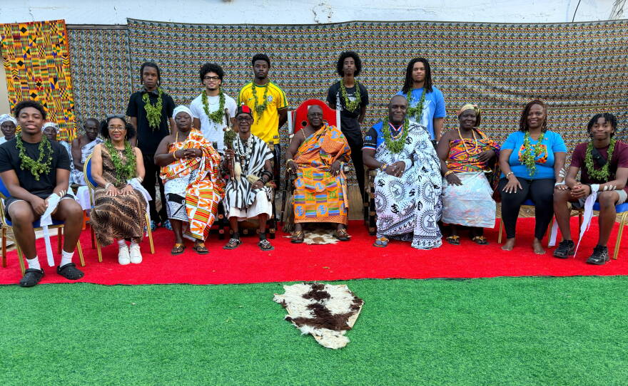 Several young men stand in a line behind a group of older people wearing colorful clothing.