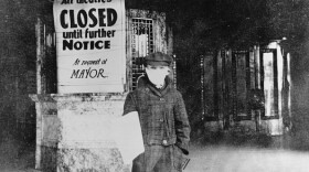 photo of a young person in a mouth-covering mask in front of a closed theater. the sign says 'all theatres closed until further notice at request of mayor.'