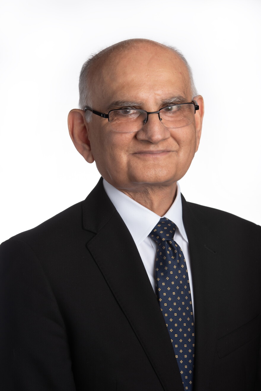 An older man wearing glasses,  poses for a professional headshot against a white background.