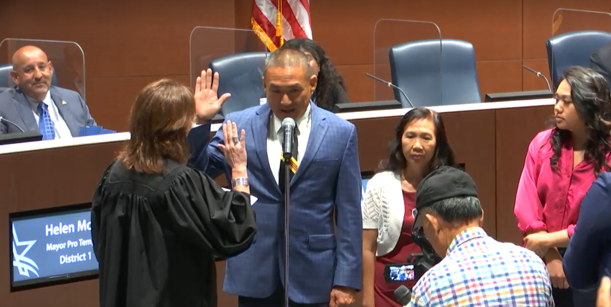 Tarrant County Precinct 2 Justice of the Peace Mary Tom Curnutt wears a black judge's robe and swears in Long Pham, a claims supervisor and U.S. Army veteran, onto Arlington City Council June 28, 2022. Pham wears a dark blue suit and is holding his right hand up to mirror Curnutt and is flanked by friends and family in Arlington's City Council chamber.