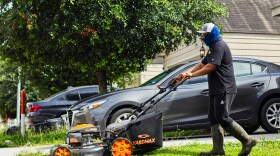 Man pushes a lawnmower across a lawn. 