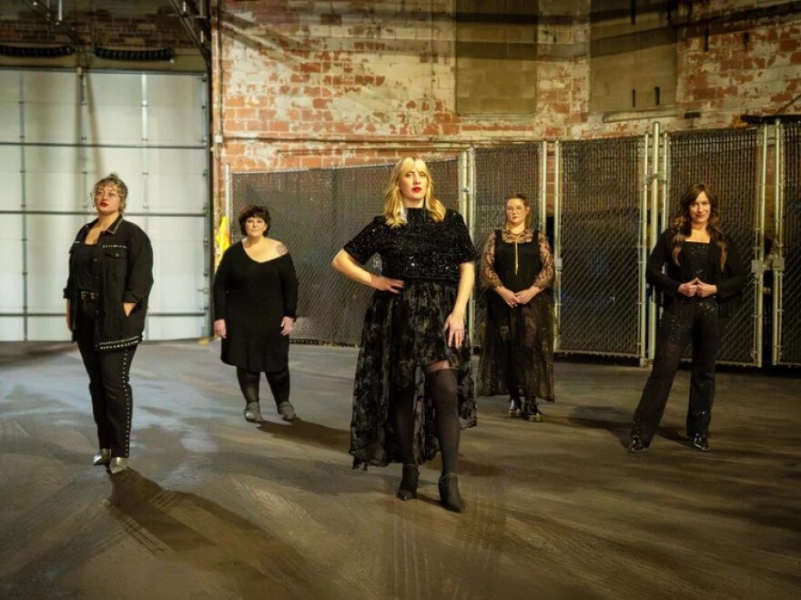 Five women wearing black posing for the camera. 