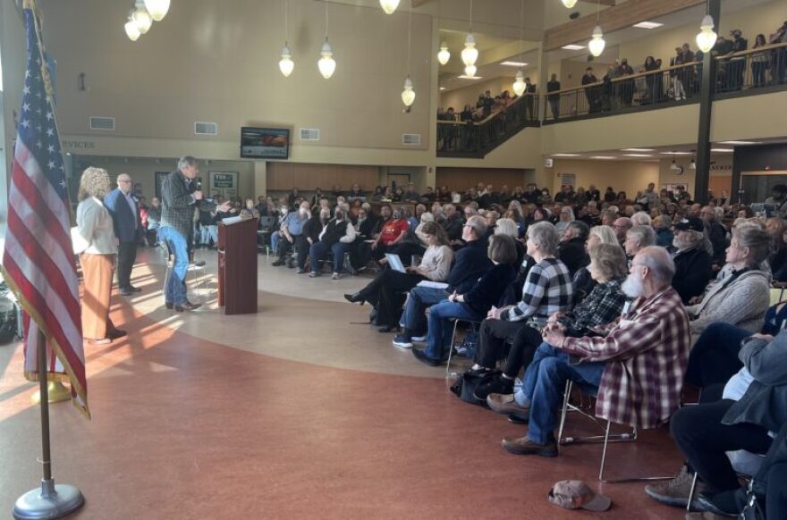 A person speaking at a microphone as audience members listen.