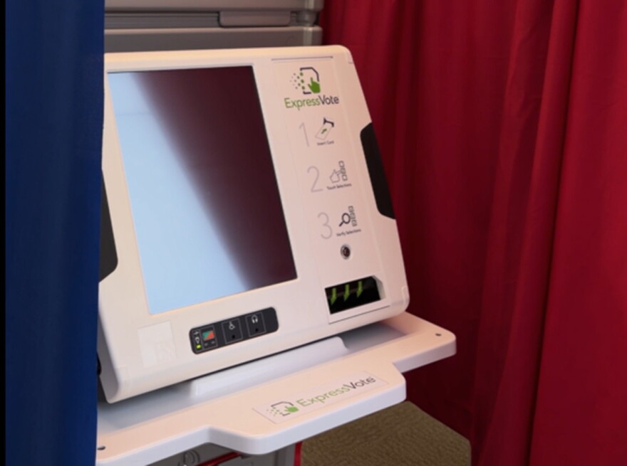 Electronic voting machine with a blank screen surrounded by a blue curtain on the left and a red curtain on the right. 