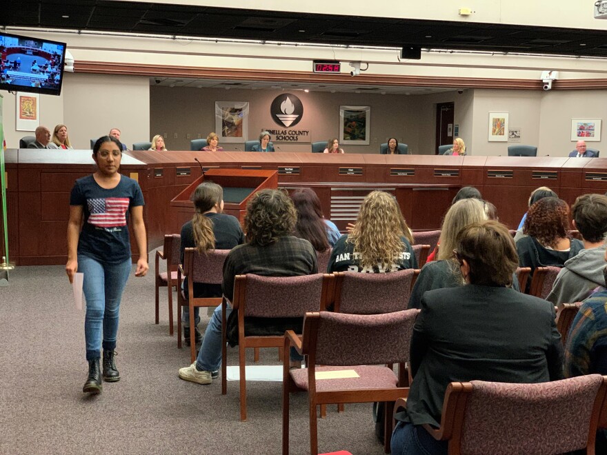 Teenager wearing American flag shirt walks away from podium at school board meeting