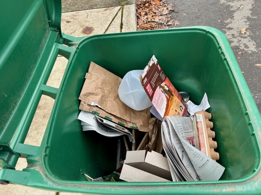 An open green bin holds newspaper, cardboard, and plastic recycling