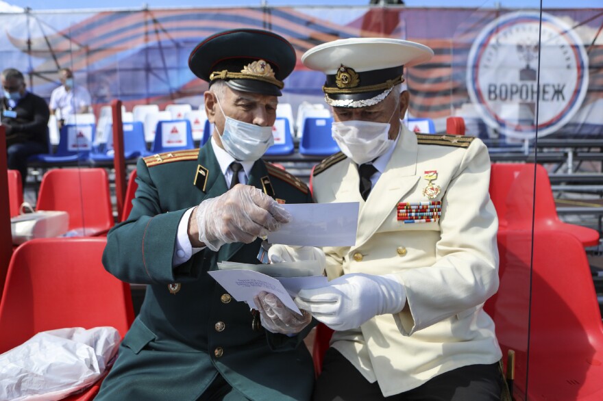 Masked World War II veteran Nikolay Borisov (left), 95, shows photos to his friend as they await a Victory Day parade. The Russian holiday, which commemorates WWII each May 9, was postponed until June 24 this year due to the pandemic. Military parades were held but fewer people turned out than usual. <em>June 24. Voronezh, Russia.</em>