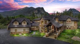 A large home sits in front of multiple mountains.