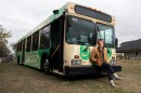 Michael Winningham sits on the front bumper of a bus painted with green images and the word "junkyard" in all caps.