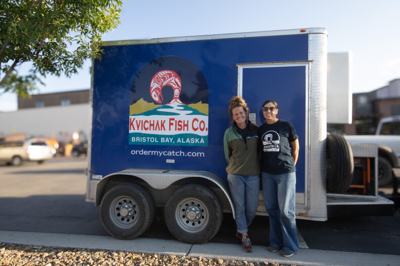 Two woman stand in front of blue trailer than says “Kvichak Fish Company” in a parking lot.