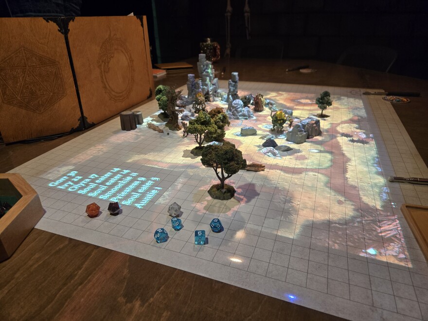 role-playing game map projected on a grid on a table. There are small figurines and dice placed along the map.