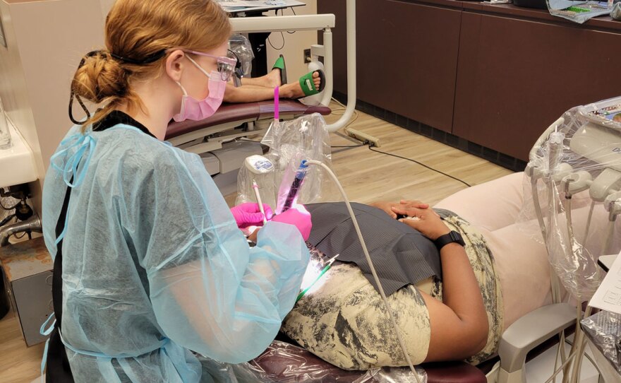 Dental student in full PPE performs a cleaning on a patient at a clinic.