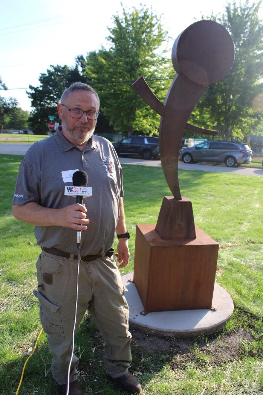 A man stands in front of a large steel sculpture. 