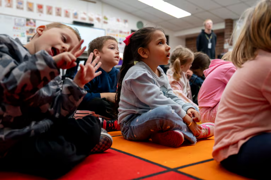 Kindergarteners sit on the floor.