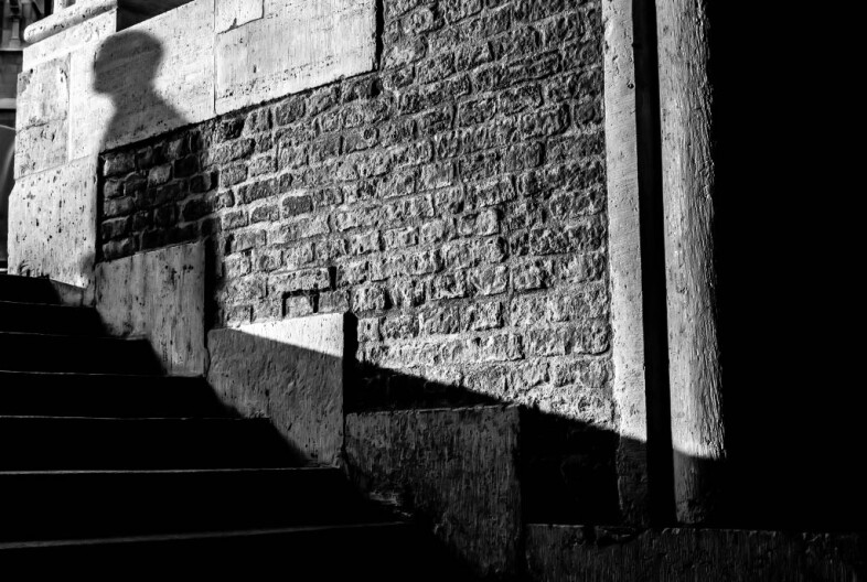 A black and white photo shows the shadow of a person on a brick and cement wall.