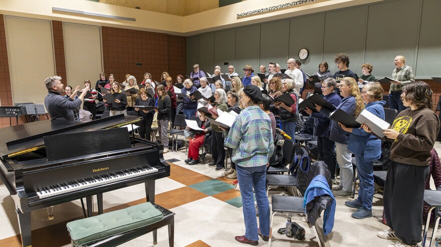 A group engages in choral practice in a small informal auditorium.