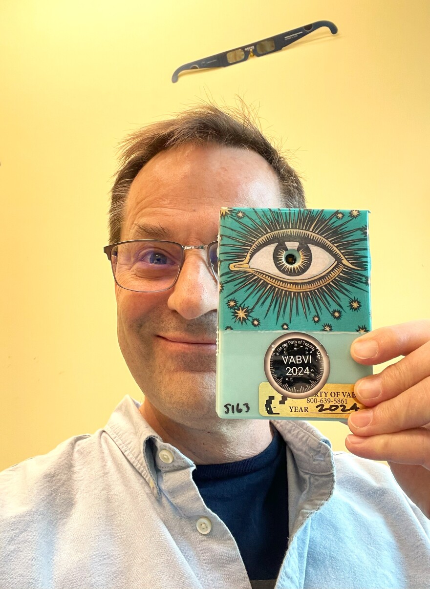 A person wearing glasses holds a light blue rectangular device with a picture of an eye up to his face. 