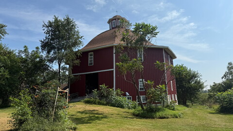 A red, octagonal barn is seen among greenery. 
