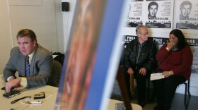 A older man sits next to a woman who is wiping tears. Behind them, posters line the wall that say "Free Efren Paredes Jr."