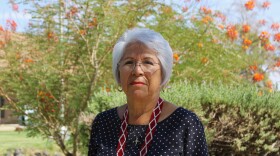 a woman wearing a beaded necklace poses for a portrait in front of flowering trees