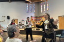 Two women sing while a band plays in the background.