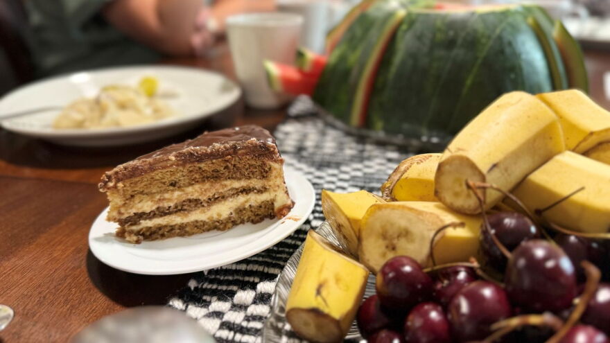 A table of food, including a chocolate cake and bananas, cherries, and watermelon.
