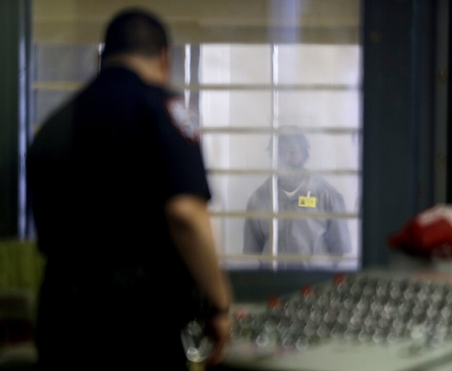 A prisoner behind bars and thick plastic looks at a corrections officer in an enhanced supervision housing unit on Rikers Island in New York.