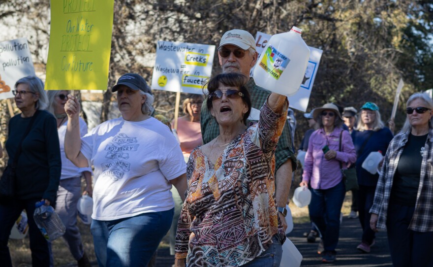 Community member Marjorie Mautz raises her gallon container with a 'Stop Lennar Corp., Save Helotes Creek' sticker on it.