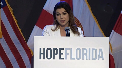 woman behind a podium that says Hope Florida speaks to an audience , american and florida flags are in the background 