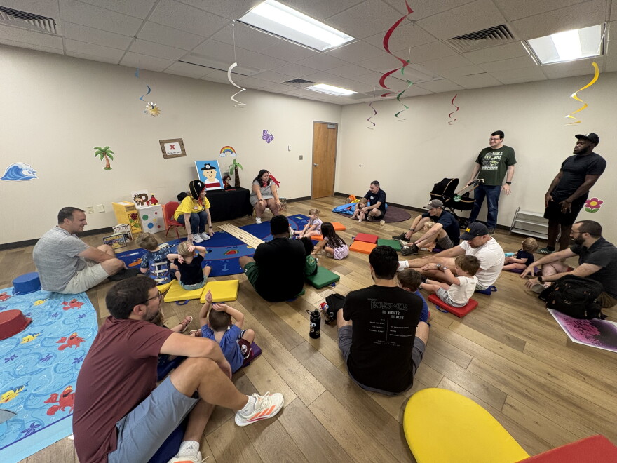 Dads and their children sit in a circle while librarians lead them in songs.